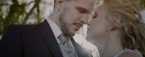 Patrick und Babsi lehnen sich zum Kuss aneinander, das Sonnenlicht fällt durch die Bäume im Weingut Bannert – ein emotionaler Moment aus ihrem Hochzeitsfilm.