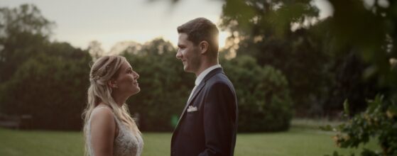 Veronika und Dominik stehen sich im Garten von Schloss Schönau gegenüber und halten sich an den Händen, festgehalten im weichen Abendlicht ihres Hochzeitsfilms.